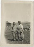 Two young people standing near a farm building, early 1900s
