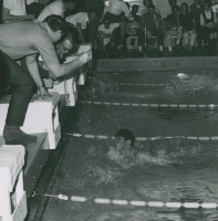 Thumbnail for 'A swimmer touches the wall as the official timers clock his time in Mountaineer Gym pool, ca. 1968.'