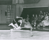 Thumbnail for 'Coeds look on as a Mountaineer grapples with his opponent in Mountaineer Gymnasium action, ca. late 1950s.'