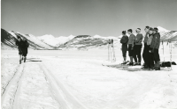Thumbnail for 'Team members look on as two competitors ski the cross country course at Rozman Hill (?) 1950s.'