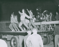 Thumbnail for 'Four WSC cheerleaders and a pep band, probably at the traditional Homecoming bonfire, 1958.'